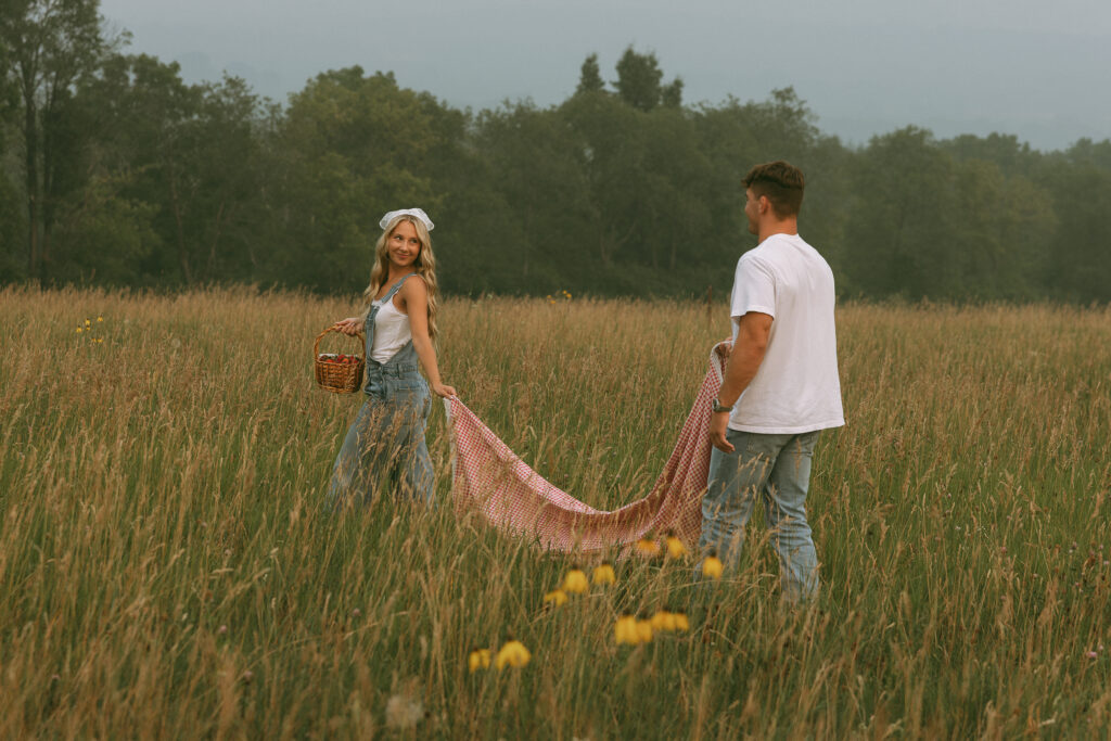 Couple setting up a red gingham picnic blanket in a grassy field for a romantic photoshoot
