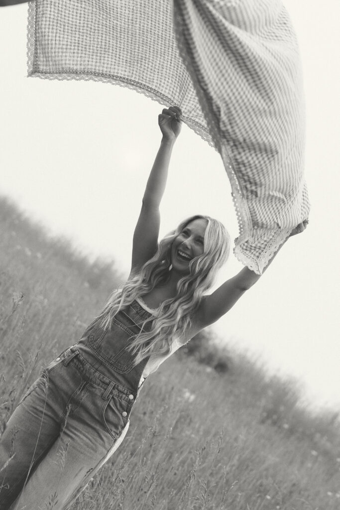 Black and white photograph of a woman laughing while holding a picnic blanket in the breeze