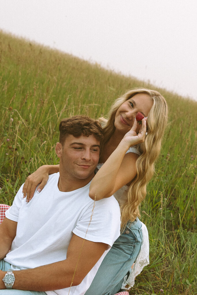 Couple sharing a quiet moment in a grassy field during a strawberry themed photoshoot